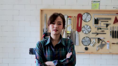Close-up portrait of young attractive carpenter standing with crossed arms in wood workshop