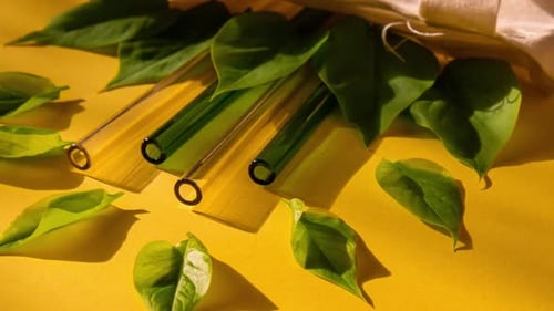 Acerque las pajitas de vidrio reutilizables sobre fondo colorido con hojas verdes en una bolsa ecológica ecológica