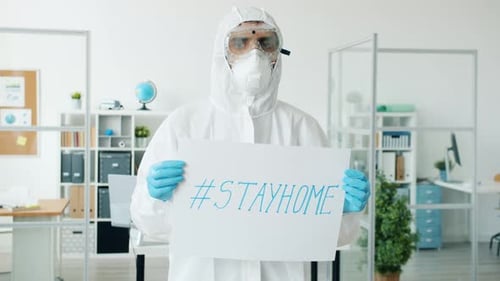 Slow Motion of Doctor in Protective Suit Standing in Empty Office with Stayhome Poster