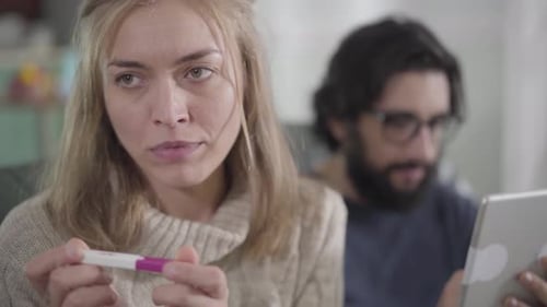 Nahaufnahme Porträt einer gefürchteten kaukasischen Frau, die als Ehemann einen positiven Schwangerschaftstest betrachtet