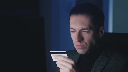 Young Man Looking at Credit Card in Dark Room