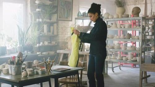 Woman Puts on Apron in Pottery Studio