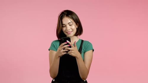 Smiling Woman Using Smartphone Against Pink Background
