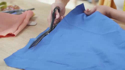 Close Up Of Female's Hand Cutting Fabric With Scissor While Working On The New Dress In The Studio
