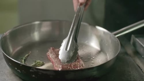 Steak Sizzling in Pan Being Turned by Chef