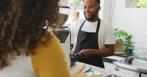 Happy african american male barista making coffee for biracial female client at cafe