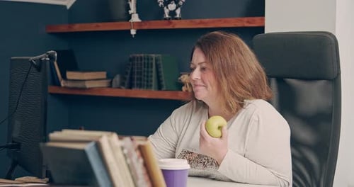 Woman Working at Computer Eating an Apple