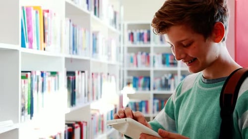 Smiling schoolboy using digital tablet in library