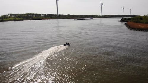 Boat Glides on River With Wind Turbines