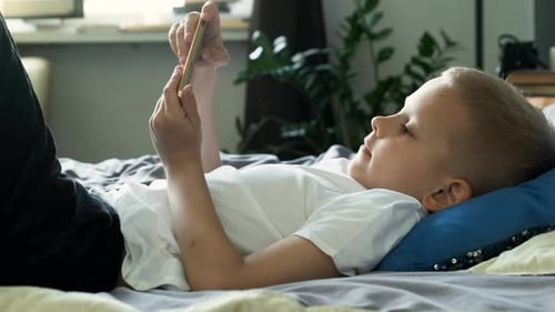 Boy Lies on Bed, Looks at Phone