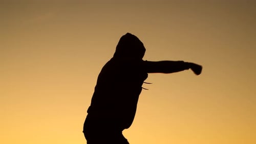 Black man athlete at hoodie struggles shadow fight background of sky, side view. Male athlete trains