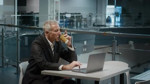 Mature Businessman Using Laptop And Drinking Coffee In Spacious Office