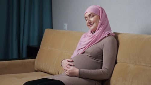 Pregnant Woman Gently Touching Baby Bump on Couch