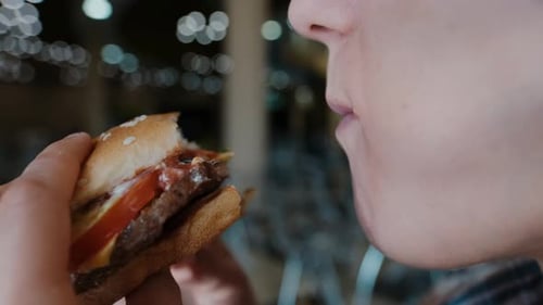 Young Hungry Woman Bites a Burger in a Fast Food Restaurant. Girl Eating a Hamburger Close Up.
