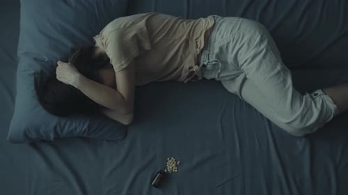 Woman Lying in Bed with Pills