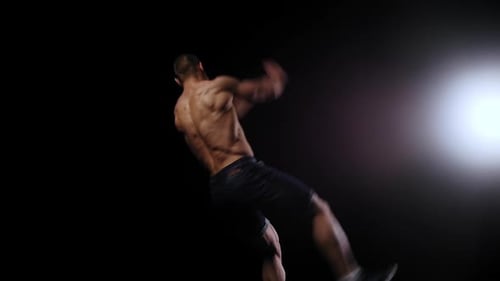 Shirtless Man Performs Gymnastic Moves Against Black Backdrop
