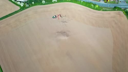 Aerial footage of a farmers field being plowed by a tractor in the summer time