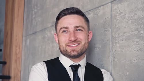 Man in Vest Smiling Against Concrete Wall