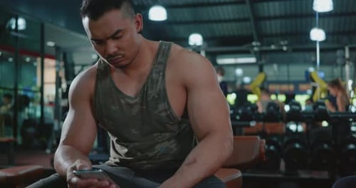 Muscular Man Using Phone in Modern Gym