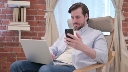 Man Works From Home on Laptop and Phone