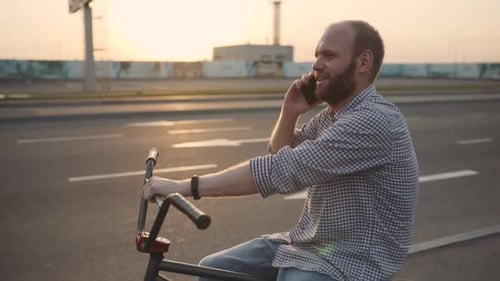 Young Man with Bmx Bicycle Uses His Phone at Sunset on the Street