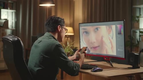 Asian Male Digital Editor Using Mobile Phone While Works In Photo Editing Software