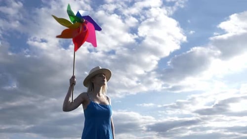 Girl in hat and blue dress with pinwheel on rural road