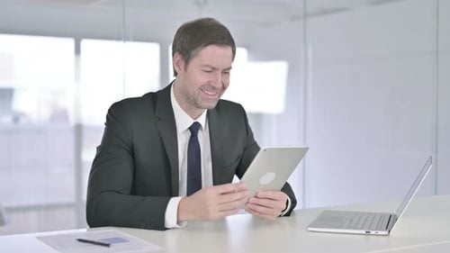Middle Aged Businessman Doing Video Chat on Tablet in Office