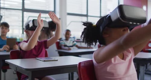 Diverse schoolchildren sitting in classroom wearing and using virtual reality glasses