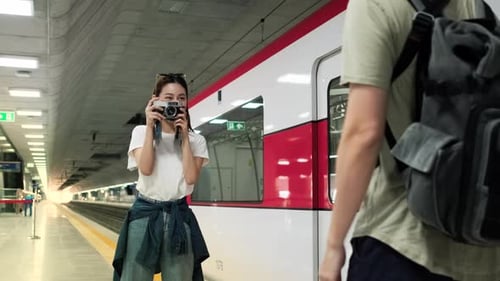 Asian female tourist take a photo with male friend at a train station platform.
