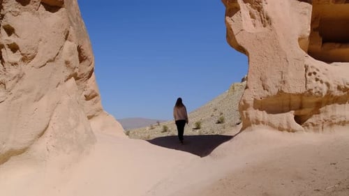Contented Woman Stands Between Two Rocks and Raises Her Hands Up