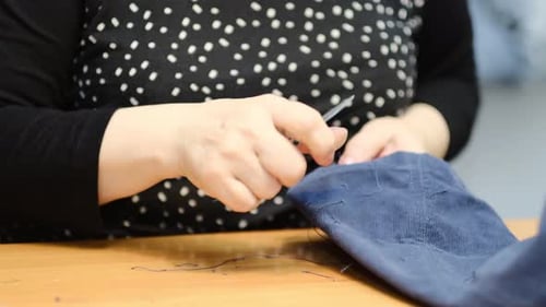 Woman Trimming Threads on Blue Textile with Scissors