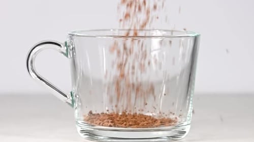 Instant Coffee Granules Pouring into Clear Glass Mug