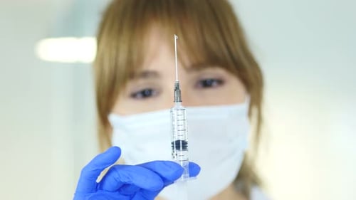 Ärztin in Maske mit Injektion, bereit zur Injektion