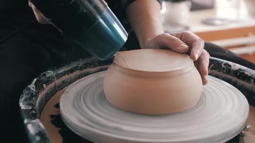 Potter Smoothing Clay Bowl with Tool on Wheel