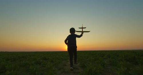 A Small Boy with a Toy Plane in His Hands Is Running Across the Field. Outdoor Games at Sunset.