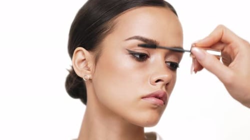 Eine hübsche Brünette hat ihre Wimpern auf weißem Hintergrund gemalt. Schönheits-Make-up