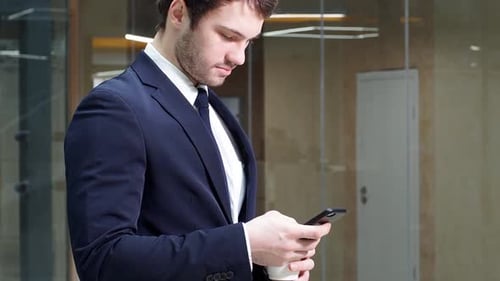 Portrait of a Young Successful Businessman Using a Smartphone in Modern Office