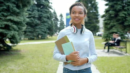 Pretty African American Girl Walking Outdoors in Park Holding Books Smiling