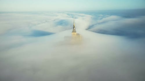 Drone Flying Away From Ethereal Mont Saint Michel Castle Spire Covered By Atmospheric Sunrise Mist