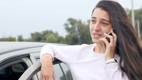Young Woman Talking on Smartphone by Car