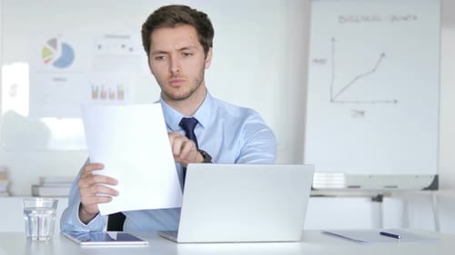 Young Adult Reviews Documents at Office Desk