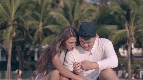 Loving Couple Sitting on Beach Looking at Phone