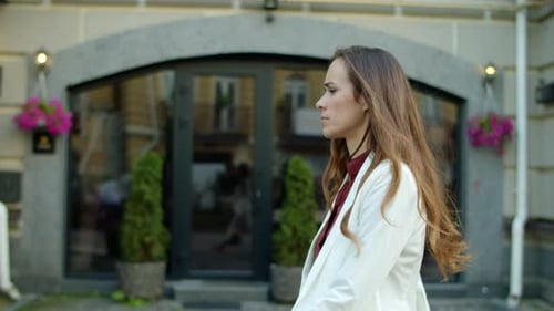 Woman Walks Past Building on City Sidewalk