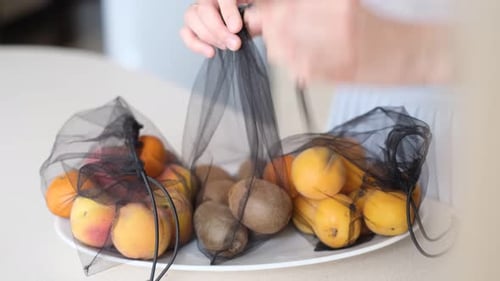 Mujer pone frutas en bolsas ecológicas en la cocina