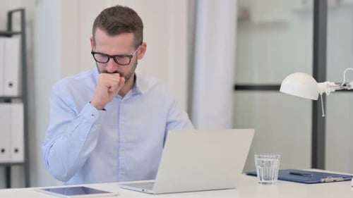 Man Working at Laptop Coughing in Office