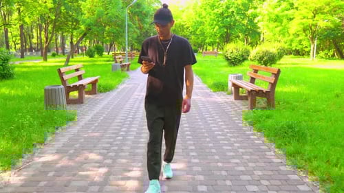 Young Adult Walks with Phone in Green Park