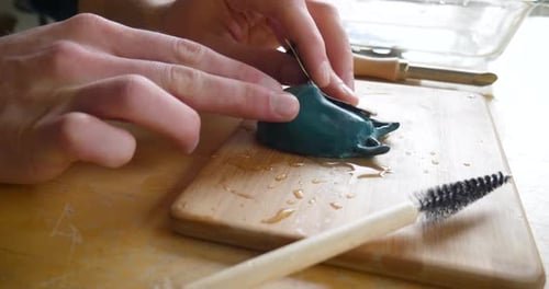 Sculptor Carves Clay Object with Tool on Board
