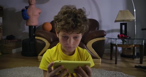 Close-up Portrait of Charming Curly-haired Boy Looking at Smartphone Screen and Smiling. Caucasian