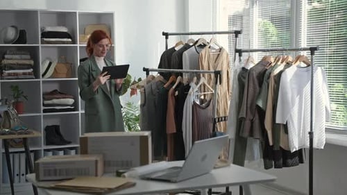 Loja de varejo: uma jovem empresária segurando um tablet na mão faz um inventário de roupas